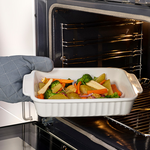 Persona colocando una fuente para hornear rectangular con verduras en el horno, usando el mango para facilitar el agarre.