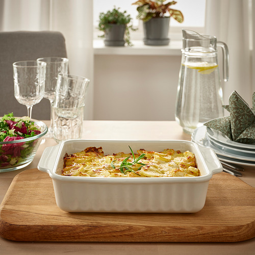 Gres blanco gratinado sobre tabla de madera, con vasos, jarra y ensaladera sobre mesa luminosa.