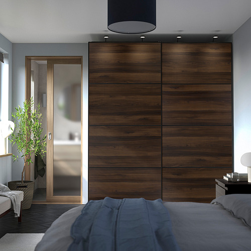 Dormitorio moderno con grandes puertas correderas de armario de efecto madera oscura, ropa de cama gris y una planta en maceta. El armario se alza sobre la cama.