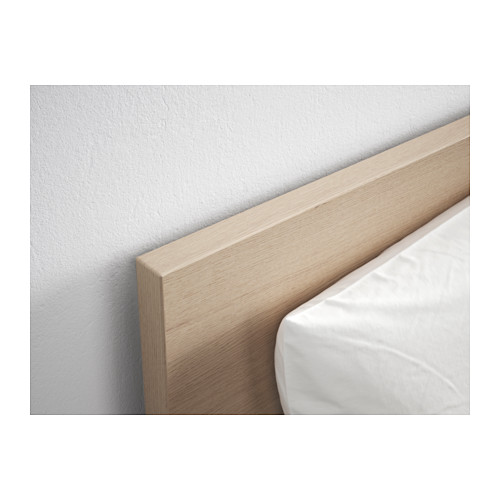 Primer plano de un cabecero de madera contra una pared blanca, con una textura de vetas de madera claras y un acabado suave.