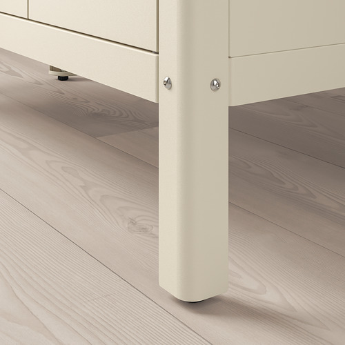 Esquina de un mueble de almacenamiento de metal blanco sobre suelo de madera clara. Pies ajustables visibles para mayor estabilidad. Diseño limpio y robusto.