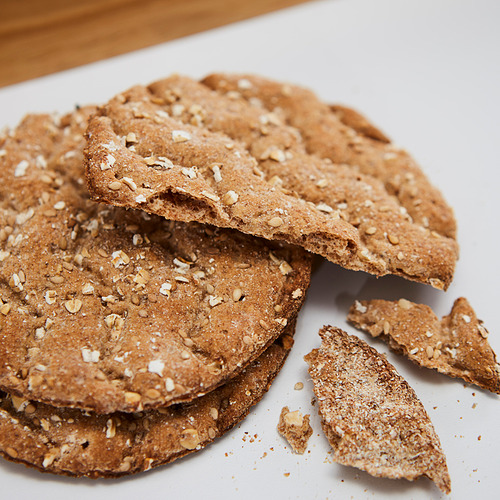 Siete galletas multigrano marrones en un plato blanco, algunas rotas.