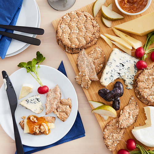 Una tabla de quesos con pan crujiente KNÄCKEBRÖD FLERKORN, varios quesos, frutas y rábanos.