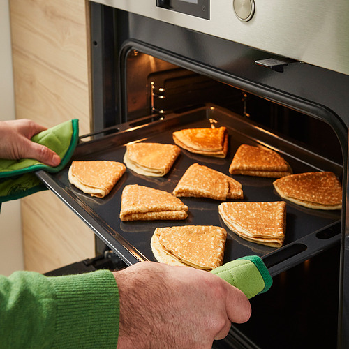 La persona saca una bandeja de panqueques PANNKAKOR dorados del horno. Guantes de cocina verdes usados.