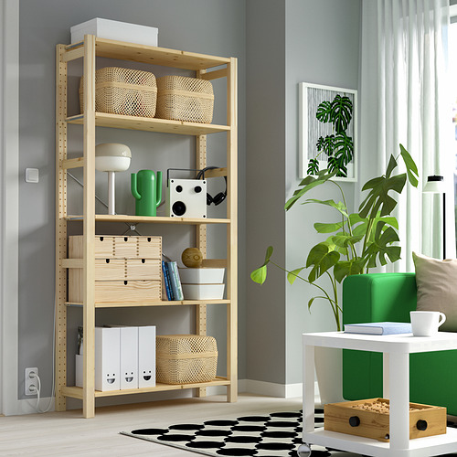 Un moderno estante de almacenamiento de pino IVAR cerca de una ventana, con cestas de mimbre, un jarrón verde, libros y artículos decorativos en una habitación acogedora.