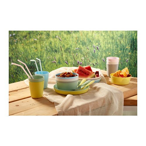 Mesa de madera con tazas de colores, platos, sandía, naranjas y tazones de comida.