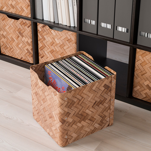 Caja de almacenamiento de bambú tejida llena de discos frente a los estantes.