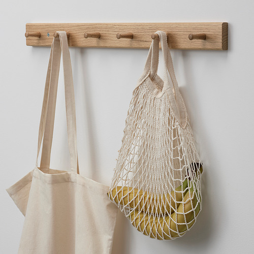 Perchero de roble de pared con tres ganchos. De los ganchos del medio cuelgan dos bolsas reutilizables, una de lona y otra de malla con frutas visibles en su interior.
