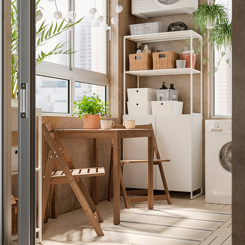 Rincón de cocina moderno con mesa, sillas, tazas, plantas y estantes NÄMMARÖ para guardar cestas y artículos de limpieza. Electrodomésticos blancos, piso de baldosas.