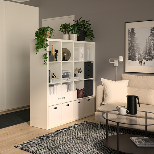 Sala de estar moderna con estantería blanca KALLAX, decoración, plantas, sofá beige, mesa de centro y marco de fotos negro.