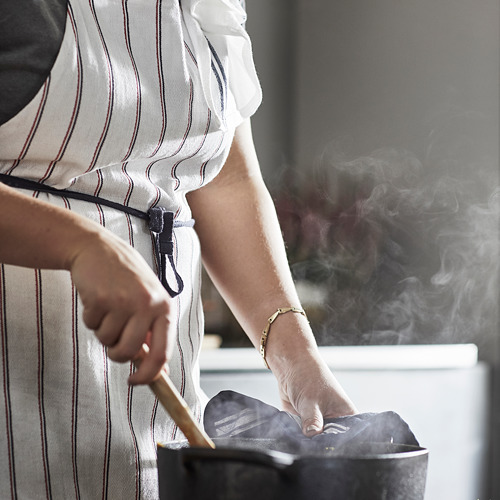 Persona con delantal de rayas blancas cocina en la estufa.