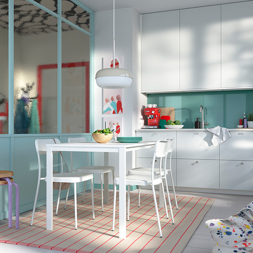 Cocina luminosa con mesa y sillas VIHALS blancas. Grandes ventanas, acentos azules, cuencos de madera y alfombras coloridas.