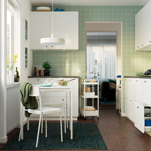 Cocina con mesa de comedor, sillas apiladas y frutero. Diseño minimalista, baldosas verdes, suelo de madera. Fondo: acogedor dormitorio.