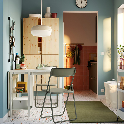 Cocina moderna con gabinetes de pino, encimera blanca y sillas plegables VIHALS. Alfombra de color neutro y suelo estampado. Paredes de color azul claro.