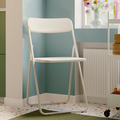 Silla plegable VIHALS blanca, delgada y moderna, se asienta perfectamente en la esquina junto a la ventana, se adapta bien al radiador y los estantes cercanos.
