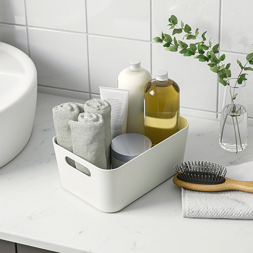 La caja de almacenamiento blanca organiza artículos de baño como toallas, botellas y un cepillo. Las asas hacen que sea fácil de transportar.