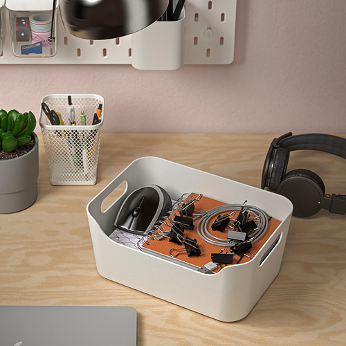 Escritorio de madera con material de oficina organizado. El contenedor blanco contiene artículos pequeños como clips y cordones. También hay auriculares y un portátil cerrado.