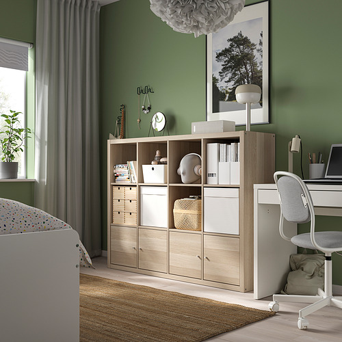 Estantería KALLAX con artículos mixtos, silla de escritorio junto a ventana verde.