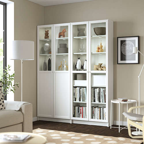 Estantería blanca BILLY en la sala de estar, alta y ancha, con libros y decoración, colocada cerca del sofá y la lámpara.