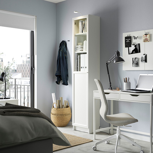 Dormitorio moderno con estantería BILLY, escritorio, computadora portátil y chaqueta azul. Incluye cesta de mimbre, alfombra y cama con ropa de cama gris.