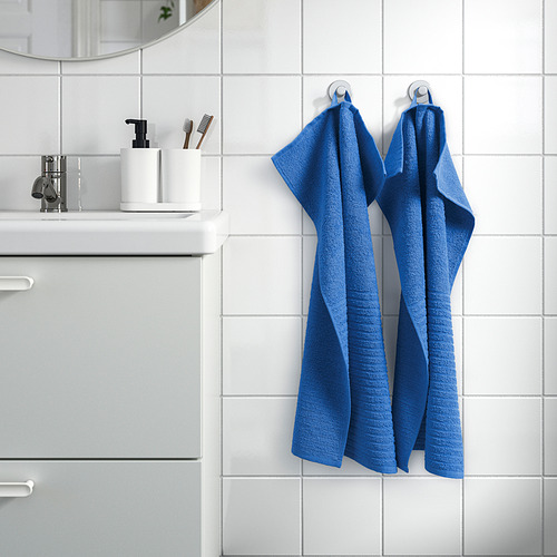 Las toallas azules cuelgan de ganchos junto a un espejo de baño con azulejos blancos, cubriendo parcialmente el lavabo.