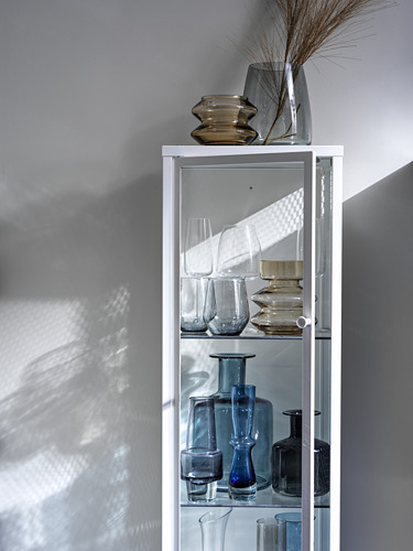 Vitrina blanca BAGGEBO con jarrones de vidrio azul y transparente y copas de vino.