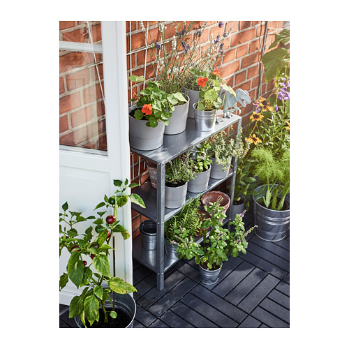 Pequeño soporte de plantas de metal para interiores / exteriores con múltiples estantes que contienen varias plantas y hierbas en macetas.