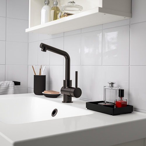 El pequeño organizador de baño negro SKOGSVIKEN se encuentra junto al lavabo, sosteniendo artículos de tocador y maquillaje.