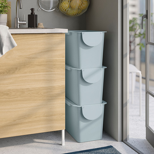 Tres contenedores apilables de color azul claro con tapa, adecuados para la clasificación o el almacenamiento de residuos, colocados junto a un armario de madera.