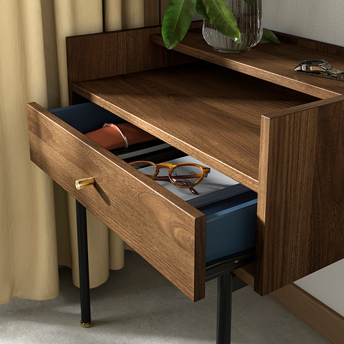 Una mesita de noche de madera llamada RÅDMANSÖ en tono nogal, con un cajón y una estantería abierta. El cajón tiene un interior azul y manijas similares al latón.