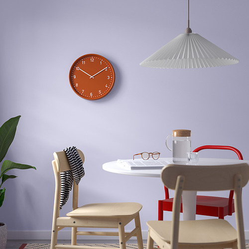 Habitación moderna con reloj BONDIS naranja, sillas de madera, mesa blanca, lámpara y plantas.