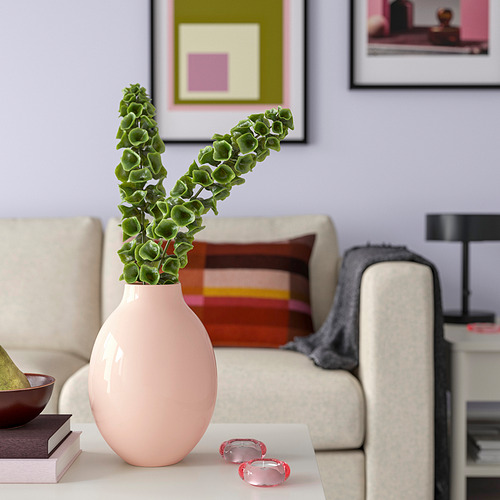 Jarrón de cerámica rosa BLODBJÖRK con ramas de plantas verdes sobre la mesa.
