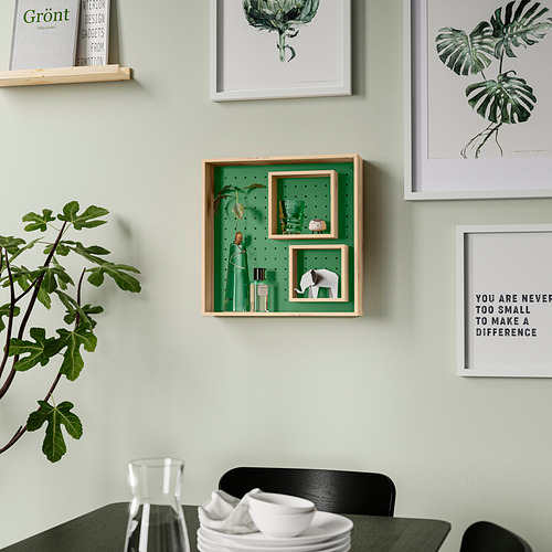 Estantería de pared verde con estantes interiores ajustables, decorada con objetos y plantas, rodeada de arte y una silla negra con vajilla.