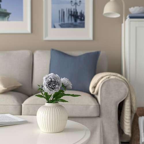 Sala de estar moderna con sofá beige, almohadas azules, jarrón PELARBJÖRK con flores y arte de pared enmarcado.