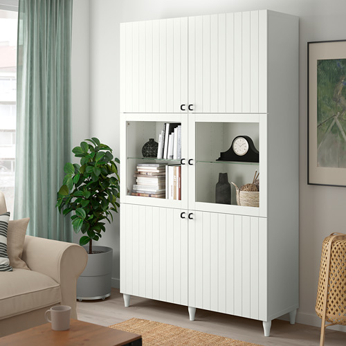 BESTÅ glass-door unit with books, vases, clock, left of chair and plant.