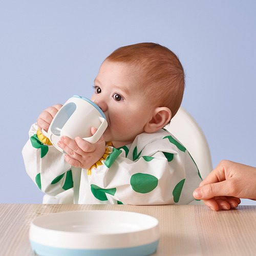 El bebé bebe de un vaso a prueba de derrames en una silla alta.
