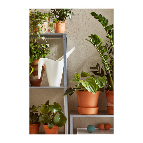 Estantería metálica con macetas de terracota, plantas y jarra blanca.