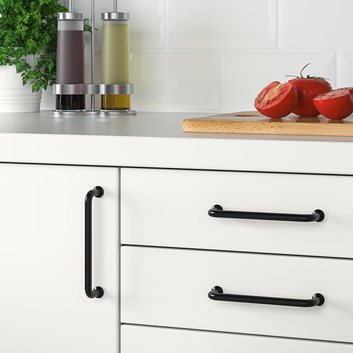 Tiradores de cajones de cocina modernos en color negro, estilo BAGGANÄS, con tornillos a la vista, colocados contra una encimera que muestra tomates y botellas.