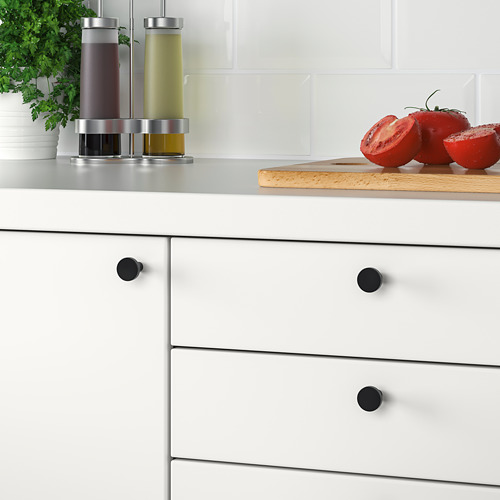 Cocina moderna con cajones blancos, con pomos negros de BAGGANÄS. Los tomates y los condimentos se exhiben en el mostrador.
