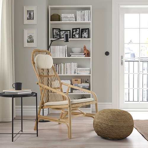 Silla de ratán natural, mesa auxiliar con libros y taza, estantería y ventana con cortinas.