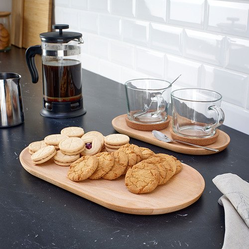 Galletas variadas en bandejas de madera ovaladas, tazas de café y prensa francesa sobre encimera negra.