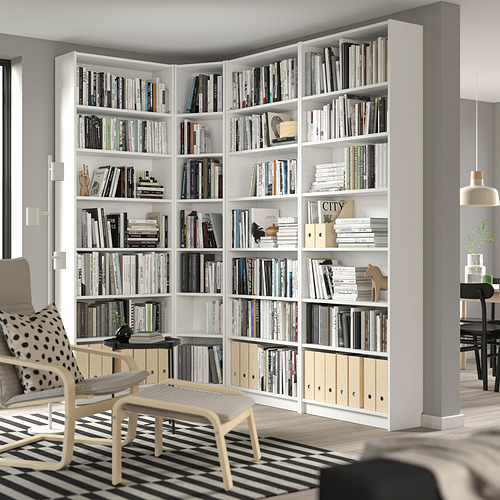 La gran estantería blanca BILLY llena la esquina, llena de libros y decoración, acompañada de una silla blanca, alfombra a rayas.