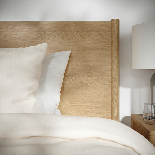 Cama moderna y minimalista con cabecero de madera clara, almohadas blancas y lámpara de noche, con diseño y materiales de calidad.