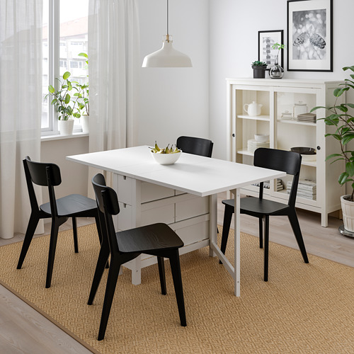 Moderna mesa abatible con 4 sillas oscuras, perfecta para espacios pequeños. Plegable, sobre alfombra beige cerca de la estantería y la ventana.