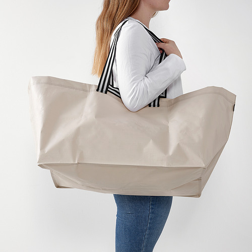 Mujer que lleva una gran bolsa de mano beige, adecuada para ir de compras o lavar la ropa.