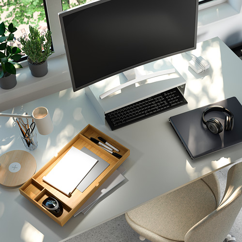 Espacio de trabajo organizado con soporte de madera para monitor, teclado, computadora portátil, auriculares y plantas.