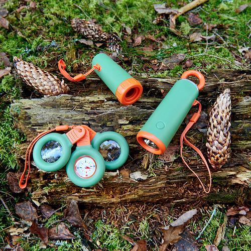 Juego de multiherramientas de camping verde y naranja con cuerda, que incluye linterna, brújula y lupa, pequeño, colocado en tronco con piñas.