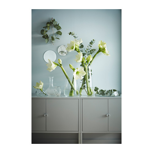 Un armario de almacenamiento gris LIXHULT con jarrones de vidrio transparente que contienen flores blancas y vegetación.