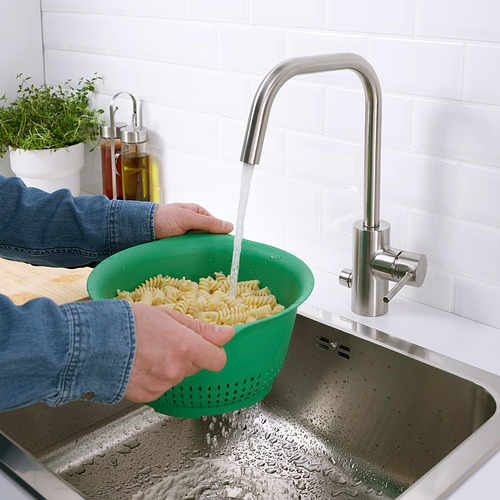 Persona enjuagando pasta cocida en un colador verde UPPFYLLD debajo del grifo de acero inoxidable.