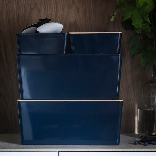 Tres cajas KUGGIS azul oscuro apiladas, la caja superior contiene gadgets electrónicos, ideales para organizar artículos de escritorio.
